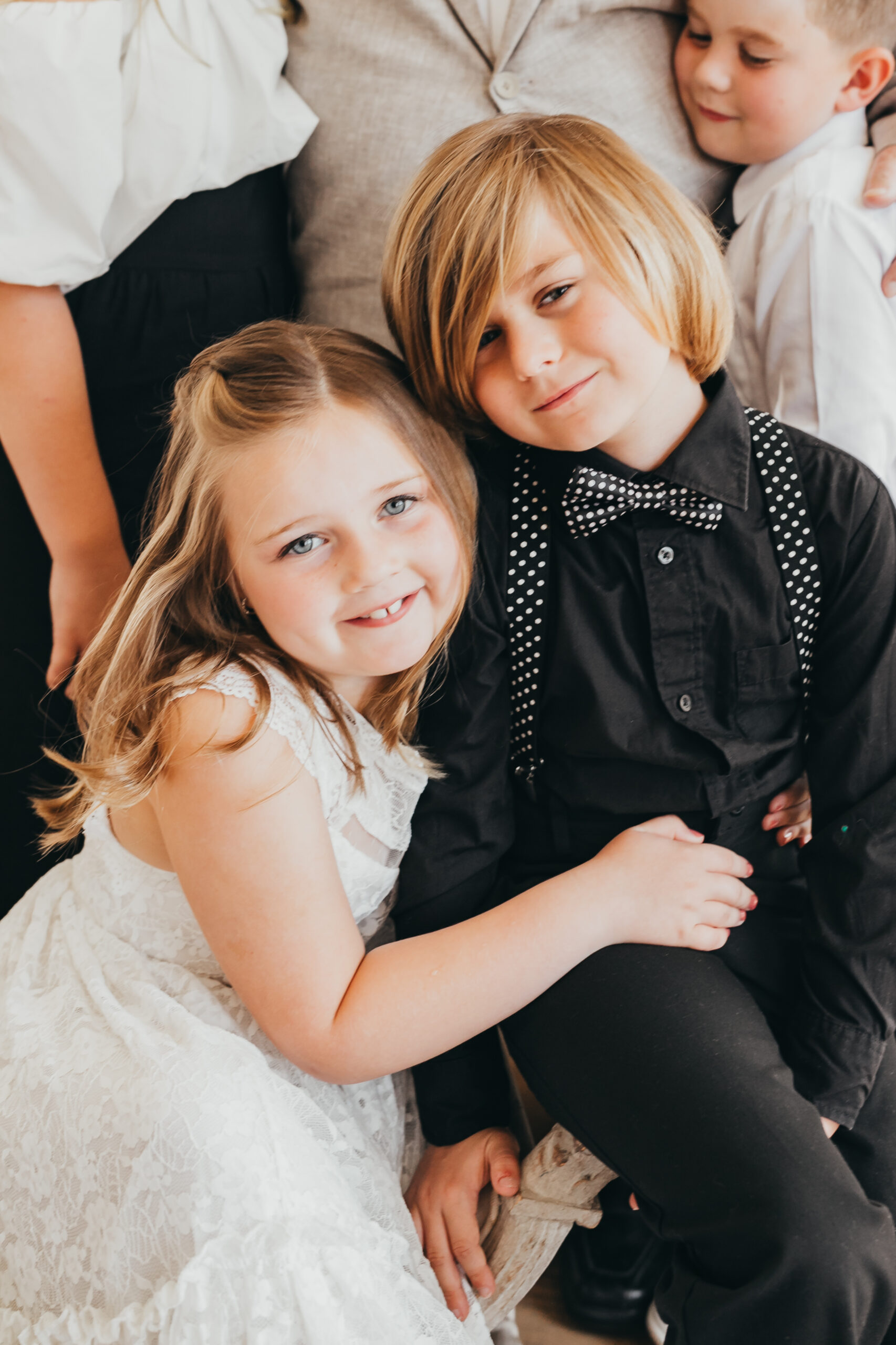 cousins hug on each other during photo session, wearing black suit and she wears a white dress.