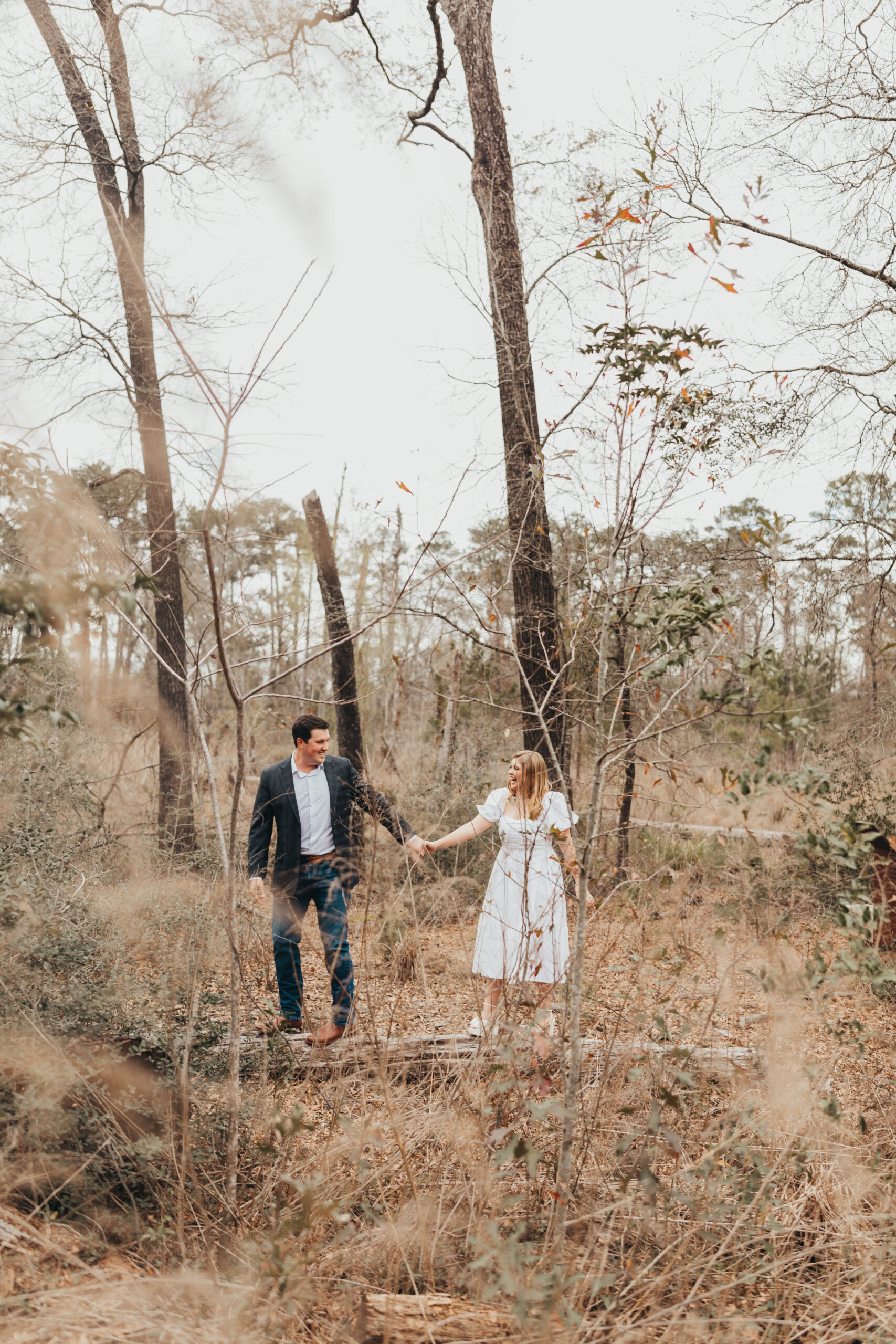 This couple holds hands while walking along a log for their engagement session at a Houston Garden Wedding Venue.